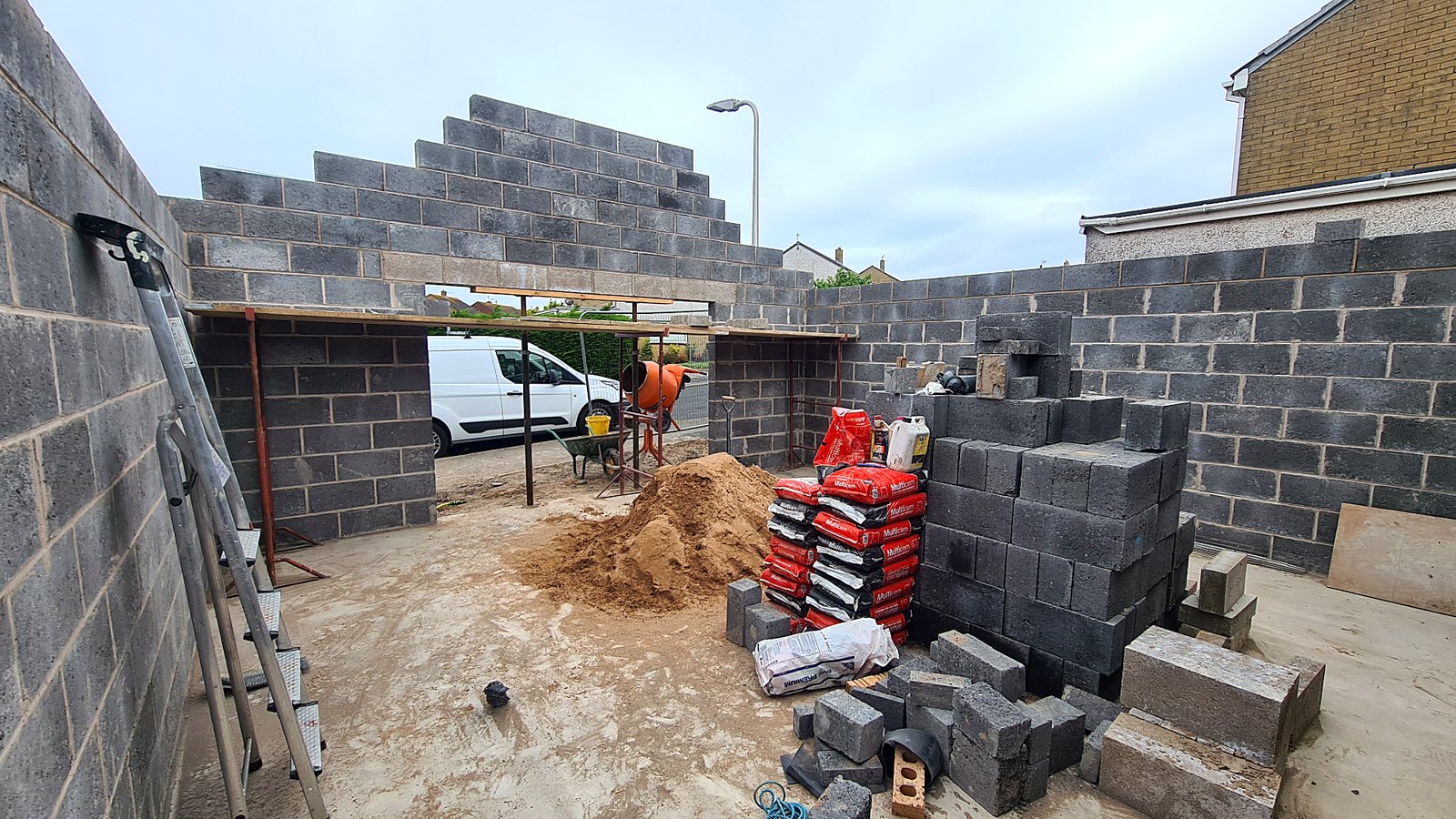 Structural blockwork walls under construction around a poured floor slab with materials stacked on site