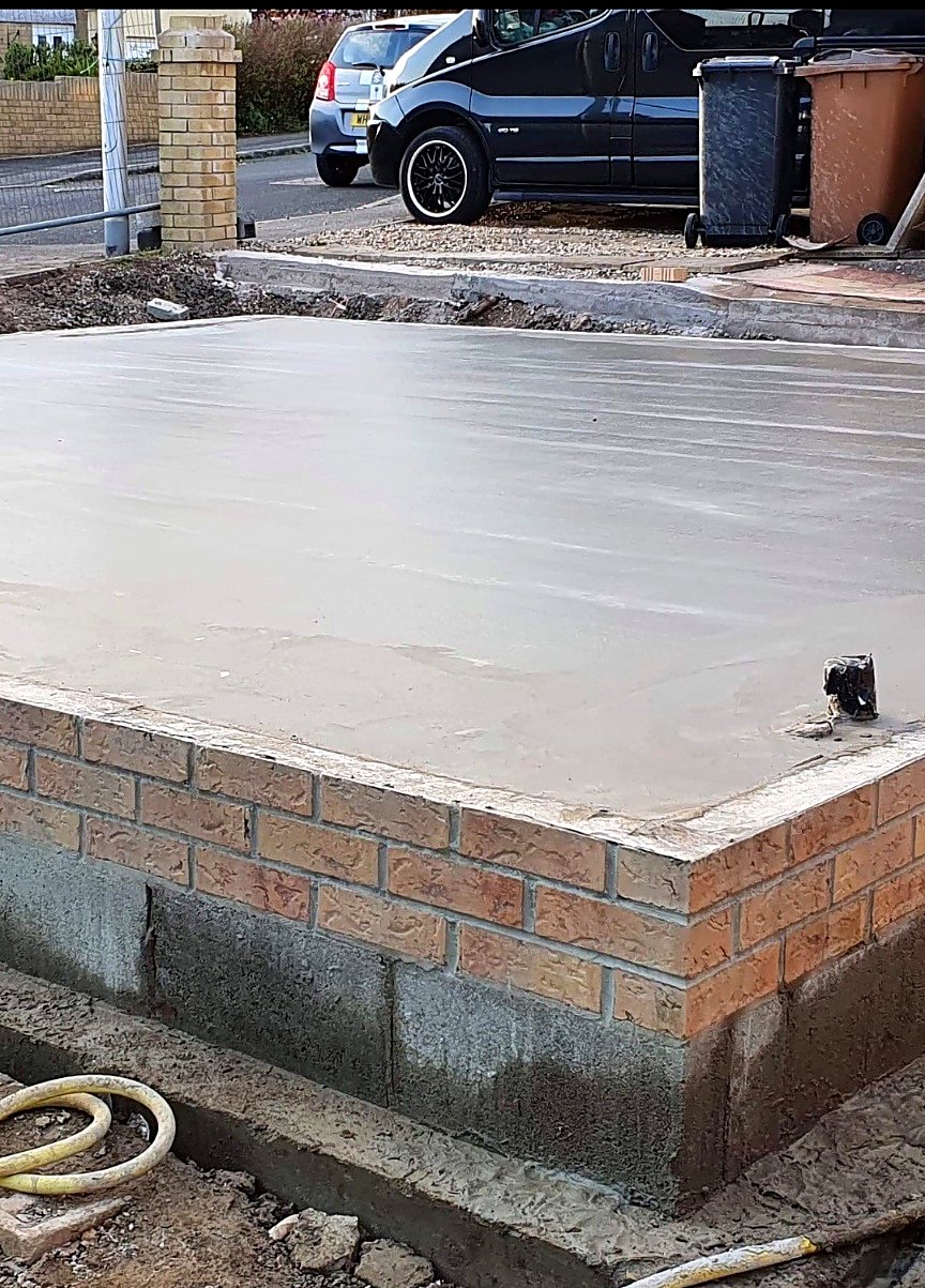Freshly finished concrete slab sitting on blockwork and brickwork beside a residential street