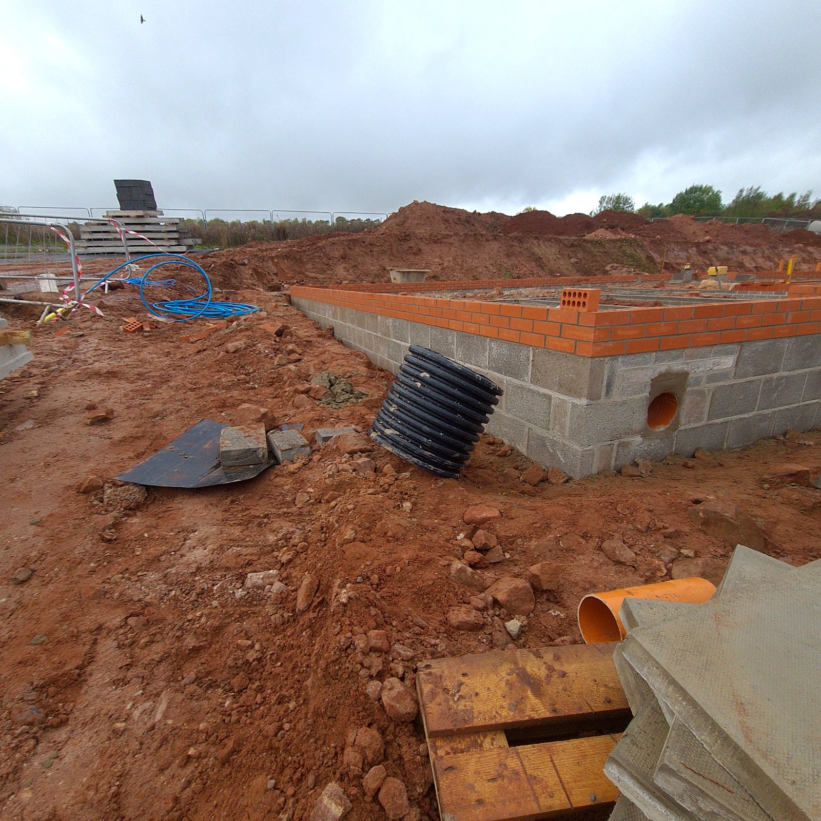 Substructure blockwork and brick course with drainage pipework and excavated ground on a construction site