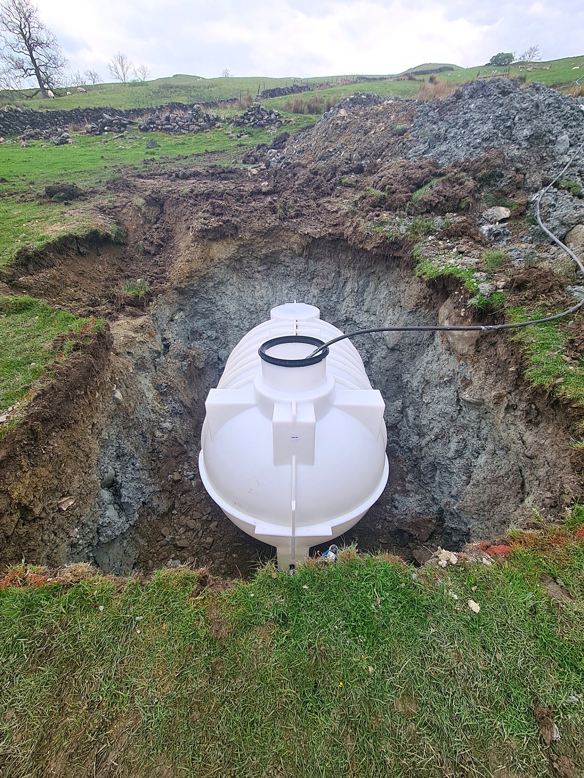 Below-ground tank being installed in an open excavation in a rural field with a connected pipe run